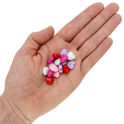 Assorted 10mm heart-shaped acrylic beads in red, pink, purple and white colors in a hand on a white background