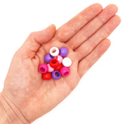Assorted large hole acrylic beads in red and pink colors in a hand on a white background