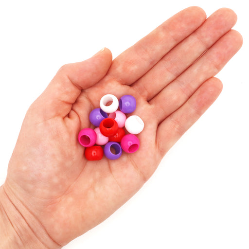 Assorted large hole acrylic beads in red and pink colors in a hand on a white background